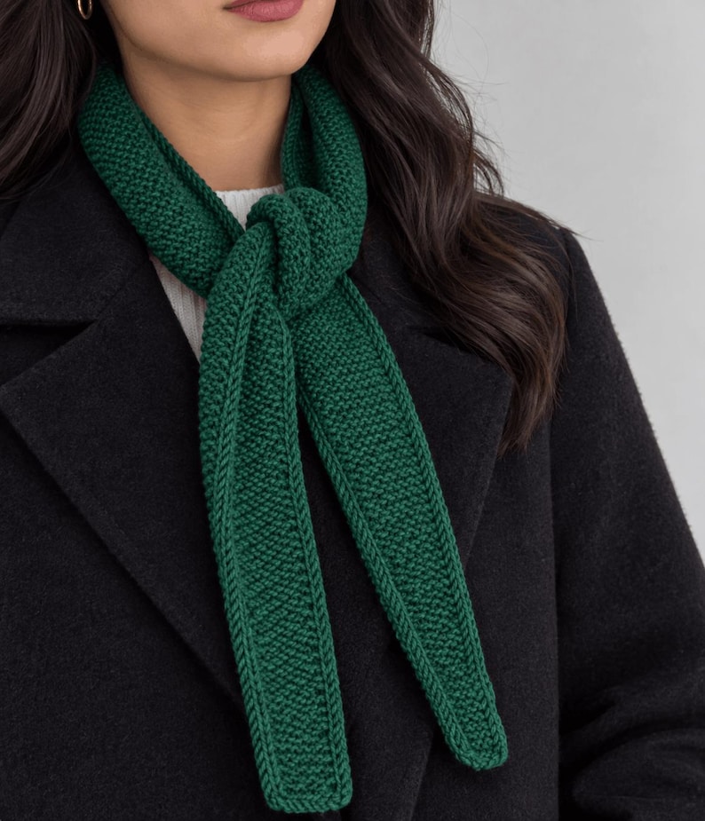 May include: A dark green knitted scarf with a textured garter stitch pattern, tied in a simple knot around the neck. The scarf is worn over a white ribbed sweater and a black wool coat, featuring clean edges and a consistent deep forest green color.