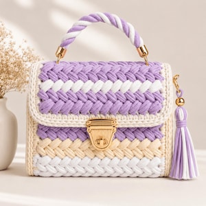 May include: A rectangular handbag crafted from braided cord in alternating stripes of lavender, white, and cream. It features a gold-tone metal push-lock closure, a twisted lavender and white cord handle, and a matching lavender and white tassel.