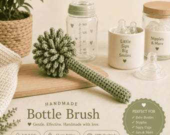 Op de afbeelding: Een saliegroene gehaakte flessenborstel met een bolvormige kop en een lange steel. De borstel wordt getoond naast een glazen babyfles met hartjes, een keramische houder met de tekst Little Sips Big Smiles en een glazen pot voor spenen.
