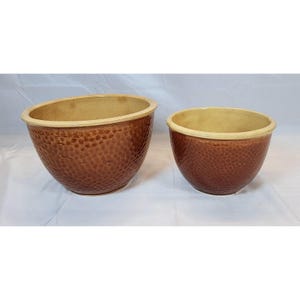 Puede incluir: Dos cuencos de cerámica marrón con una superficie texturizada y con hoyuelos. Los cuencos tienen un interior de color beige claro y un borde de color beige claro. Los cuencos son de diferentes tamaños y probablemente para uso decorativo o funcional.