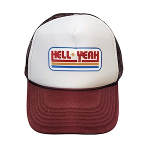 Könnte beinhalten: Burgunderfarbene und weiße Trucker-Cap mit Mesh-Rückseite und gebogenem Schirm. Die Vorderseite ist weiß mit den Worten "HELL YEAH" in einem rechteckigen Design mit roten, orangefarbenen, blauen und sternförmigen Grafiken.
