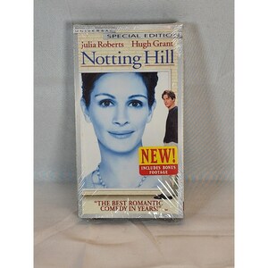 May include: Sealed VHS tape of the movie "Notting Hill" featuring Julia Roberts and Hugh Grant. The cover has a large image of Julia Roberts' face, with Hugh Grant in a smaller image. A "NEW!" sticker is visible, along with the text "THE BEST ROMANTIC COMEDY IN YEARS!"