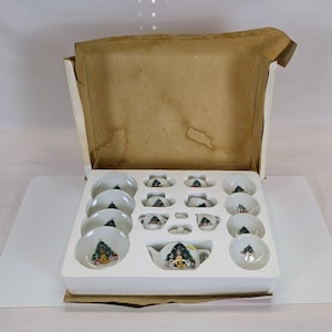 May include: A miniature porcelain tea set featuring a Christmas tree and teddy bear motif, including a teapot, cups, and saucers, housed in a tan cardboard box with a white styrofoam insert that has molded compartments for each individual piece.