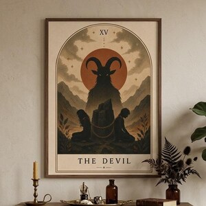 Puede incluir: Una lámina de arte enmarcada titulada THE DEVIL, que muestra una figura central con cuernos en silueta frente a un gran sol rojo, con dos figuras encadenadas a una roca. La ilustración está dentro de un borde arqueado con el número romano XV.