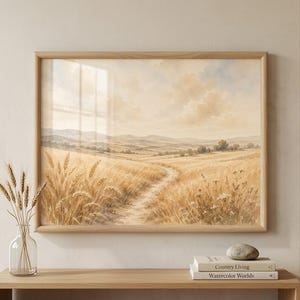 Op de afbeelding: Een ingelijste landschapsafdruk met een goudkleurig tarweveld en een kronkelend zandpad dat naar verre heuvels leidt onder een zachte, bewolkte lucht. Het kunstwerk zit in een lichthouten lijst en toont een sereen, warm getint landelijk tafereel.