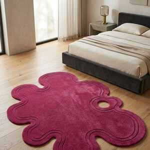 May include: A deep magenta area rug with an irregular, organic, amoeba-like shape featuring a cut-out hole near one edge and a double-line embossed border that follows the perimeter of the rug's unique, wavy, and rounded silhouette.