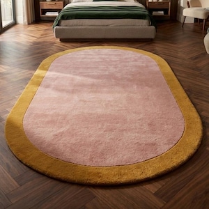 Luxury blush pink oval rug with mustard gold border placed in modern wooden floor living room, soft minimalist Scandinavian style carpet for aesthetic home decor.