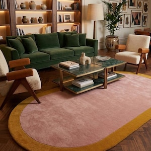 May include: A stylish living room with a green velvet sofa, cream armchairs, and a pink rug with a yellow border. A coffee table with a green marble top is in the centre. Bookshelves and framed art complete the decor.