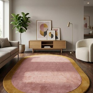 Puede incluir: Una alfombra ovalada rosa y dorada en un sal&oacute;n. La alfombra tiene un centro rosa suave con un borde dorado. La habitaci&oacute;n tambi&eacute;n cuenta con un mueble de madera, obras de arte, un sof&aacute;, una planta y un sill&oacute;n blanco.