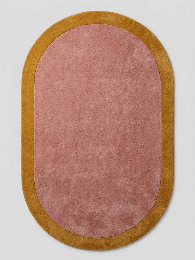Puede incluir: Una alfombra ovalada con un centro rosa empolvado y un borde amarillo dorado. La alfombra tiene una textura suave y afelpada, y la combinaci&oacute;n de colores crea una est&eacute;tica c&aacute;lida. Adecuada para salones y dormitorios, mide unos 150 cm x 90 cm.