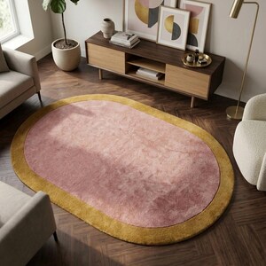 Puede incluir: Alfombra ovalada con centro rosa y borde amarillo mostaza. La alfombra est&aacute; colocada sobre un suelo de madera oscura. La habitaci&oacute;n cuenta con muebles y obras de arte modernos. Las dimensiones de la alfombra no son visibles.