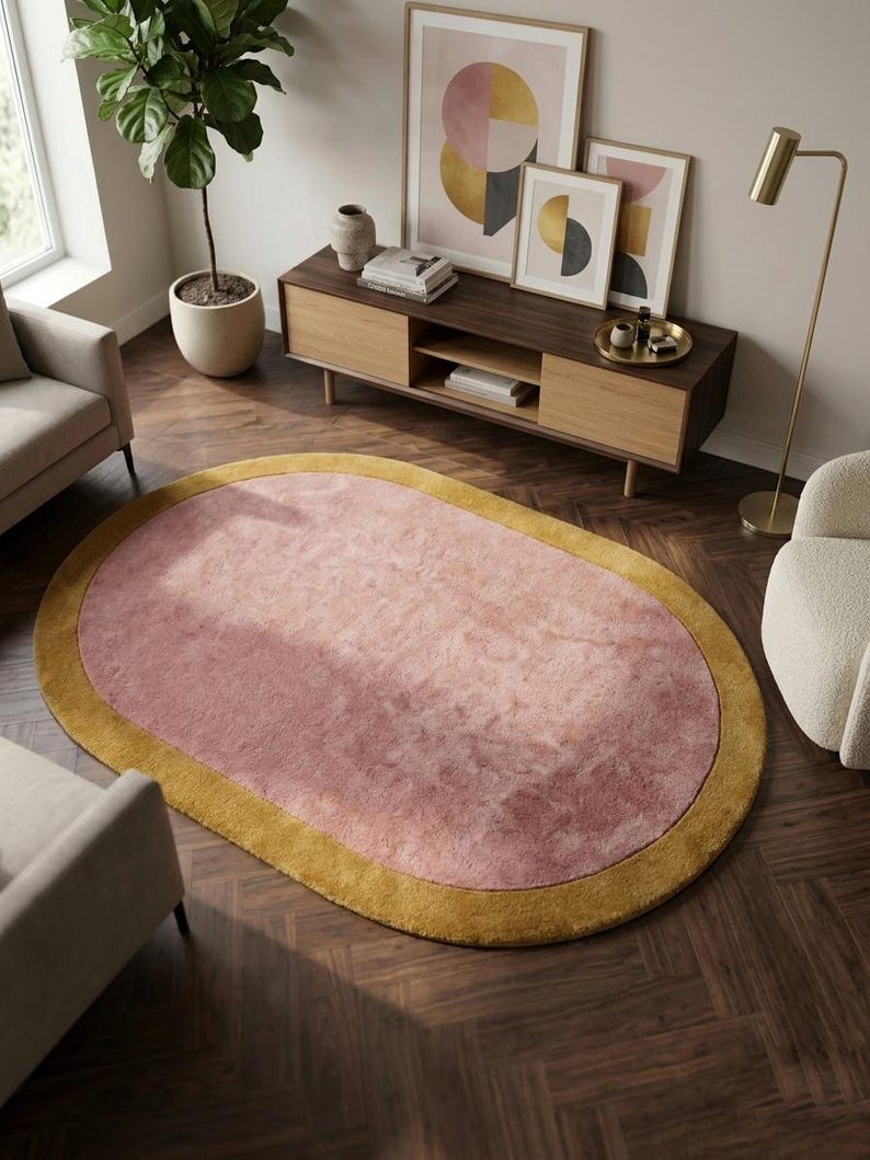 Puede incluir: Alfombra ovalada con centro rosa y borde amarillo mostaza. La alfombra est&aacute; colocada sobre un suelo de madera oscura. La habitaci&oacute;n cuenta con muebles y obras de arte modernos. Las dimensiones de la alfombra no son visibles.