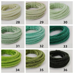 May include: Nine coiled, plush hair ties in shades of green, from pale to deep. Each tie is a different colour, with numbers 28 to 36 printed below each. The ties are made of a soft, velvety material.
