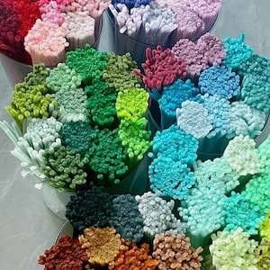 May include: A selection of colourful craft supplies, featuring bundles of small, textured sticks in shades of pink, blue, green, and brown. The sticks are arranged in clear containers, creating a vibrant display.