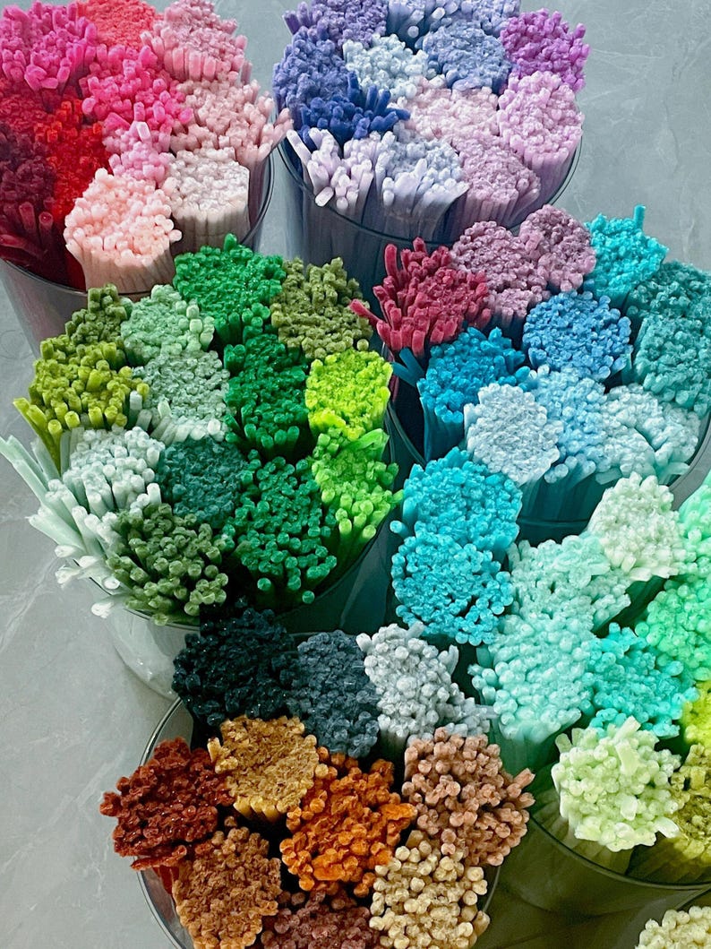 May include: A selection of colourful craft supplies, featuring bundles of small, textured sticks in shades of pink, blue, green, and brown. The sticks are arranged in clear containers, creating a vibrant display.