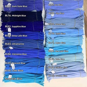 May include: A collection of fuzzy pipe cleaners arranged in two columns, featuring various shades of blue labeled with codes and names including BL18 Dark Slate Blue, BL16 Midnight Blue, BL01 Sapphire Blue, BL07 Ice Blue, and BL15 Breeze Blue.