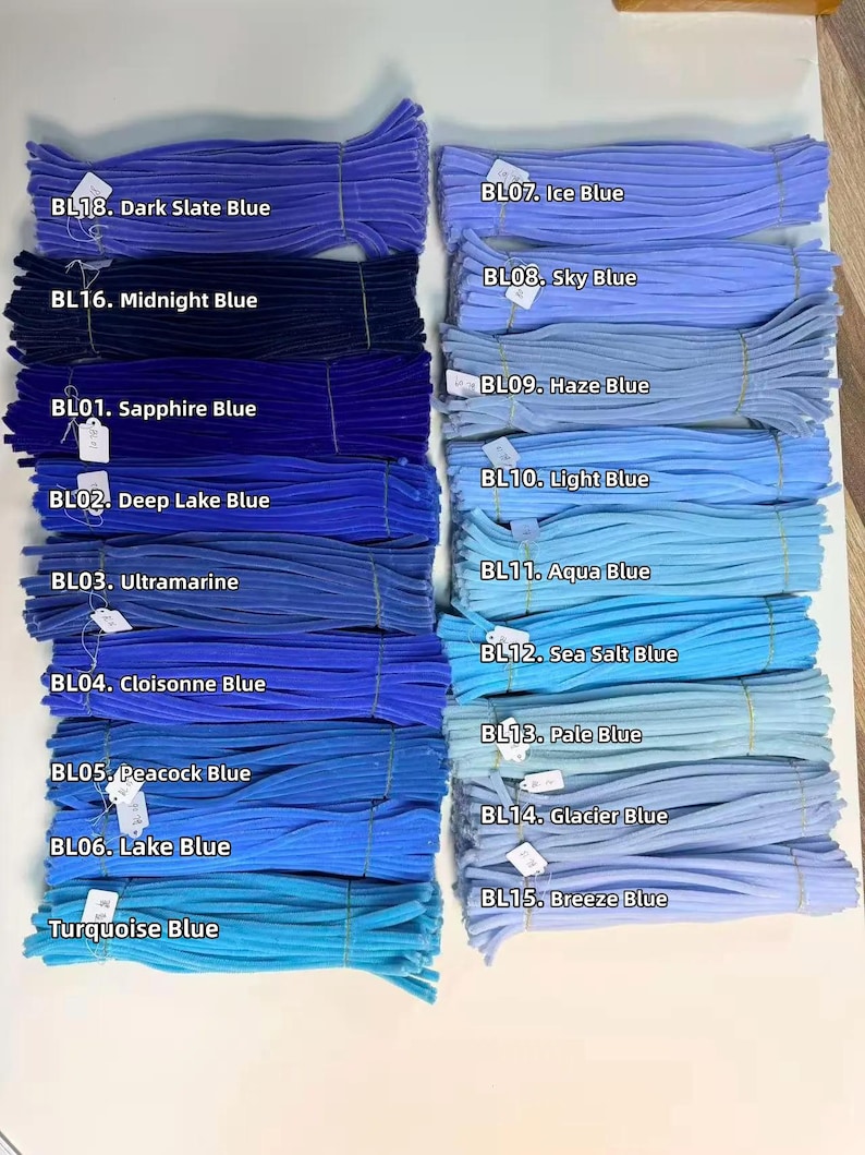 May include: A collection of fuzzy pipe cleaners arranged in two columns, featuring various shades of blue labeled with codes and names including BL18 Dark Slate Blue, BL16 Midnight Blue, BL01 Sapphire Blue, BL07 Ice Blue, and BL15 Breeze Blue.
