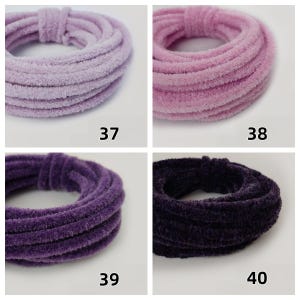 May include: Four skeins of soft, plush yarn in shades of lavender, pink, purple, and dark purple. Each skein is coiled into a circular shape. Numbers 37, 38, 39, and 40 are printed below each yarn colour.
