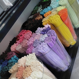 May include: A selection of colourful craft supplies, featuring bundles of thin, flexible plastic rods in various shades. The rods are displayed in clear cylindrical containers, showcasing hues of pink, purple, yellow, orange, and green. The image is well-lit, highlighting the vibrant colours.