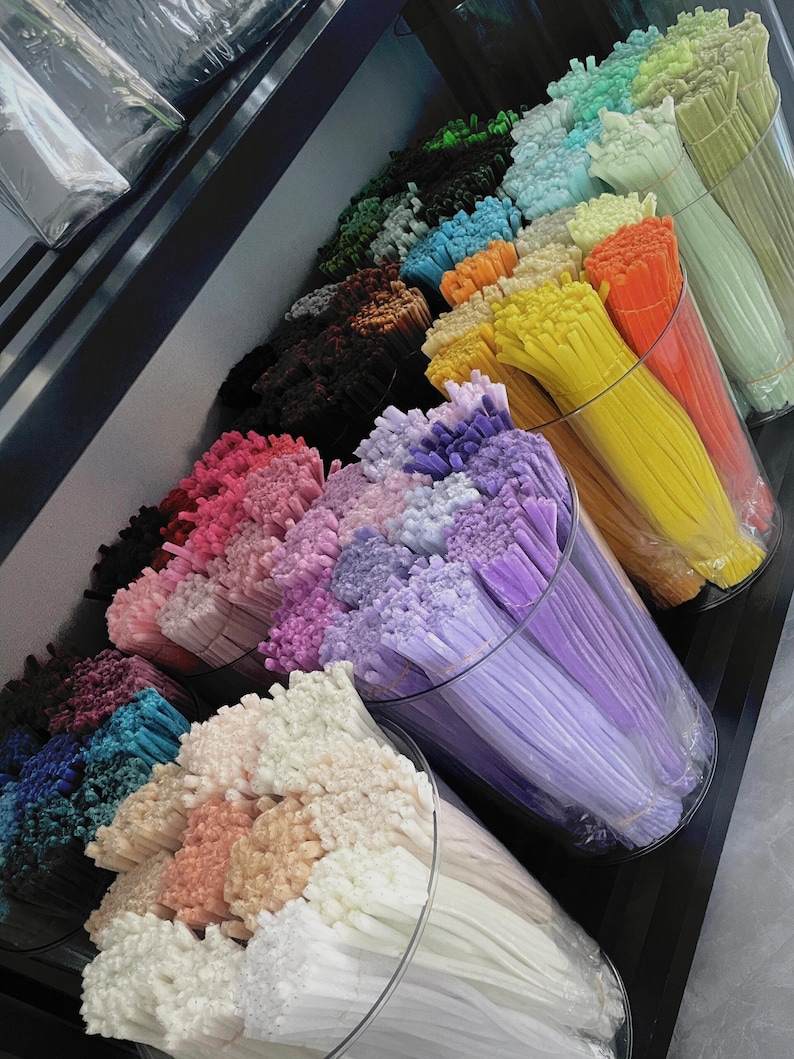 May include: A selection of colourful craft supplies, featuring bundles of thin, flexible plastic rods in various shades. The rods are displayed in clear cylindrical containers, showcasing hues of pink, purple, yellow, orange, and green. The image is well-lit, highlighting the vibrant colours.