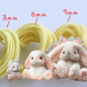 Puede incluir: Primer plano de tres animales de peluche: un oso, un conejito y un conejo más grande con un lazo rosa. La imagen también muestra un cordón amarillo en tamaños de 3 mm, 6 mm y 9 mm. Los juguetes son blancos y rosas.