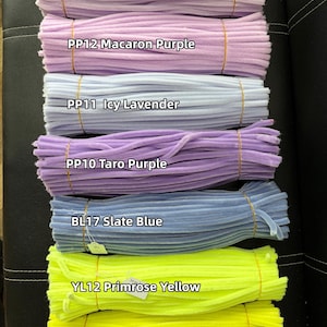 May include: Seven bundles of fuzzy pipe cleaners arranged horizontally. Colors include PP13 Light Purple, PP12 Macaron Purple, PP11 Icy Lavender, PP10 Taro Purple, BL17 Slate Blue, YL12 Primrose Yellow, and YL11 Pastel Yellow, each secured with a thin band.
