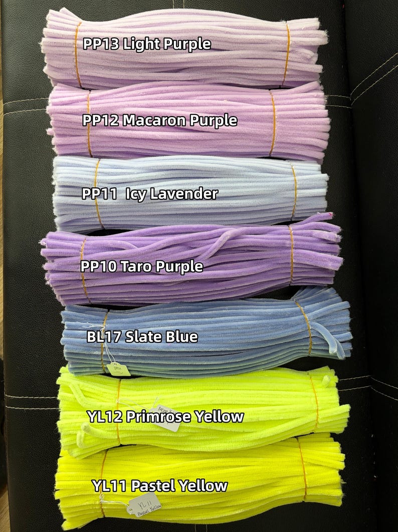May include: Seven bundles of fuzzy pipe cleaners arranged horizontally. Colors include PP13 Light Purple, PP12 Macaron Purple, PP11 Icy Lavender, PP10 Taro Purple, BL17 Slate Blue, YL12 Primrose Yellow, and YL11 Pastel Yellow, each secured with a thin band.