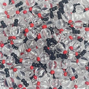 May include: Close-up of clear, round beads with red and black accents. The beads are strung together, creating a textured and layered effect. The clear beads have a reflective quality, and the red and black beads add pops of color.