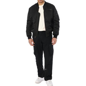 Puede incluir: Una chaqueta bomber negra con cierre de cremallera, usada sobre una camiseta crema. El conjunto incluye pantalones cargo negros con m&uacute;ltiples bolsillos y cremalleras en los tobillos. Zapatillas blancas completan el look.