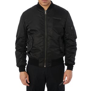 Puede incluir: Chaqueta bomber negra con cuello, pu&ntilde;os y dobladillo de canal&eacute;. La chaqueta tiene cierre de cremallera frontal, m&uacute;ltiples bolsillos y un peque&ntilde;o detalle de parche en el pecho. La chaqueta est&aacute; hecha de un material liso y brillante.