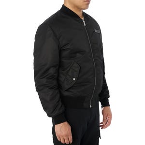 Puede incluir: Chaqueta bomber negra con cremallera, pu&ntilde;os de canal&eacute; y un peque&ntilde;o bolsillo en la manga izquierda. La chaqueta tiene un peque&ntilde;o parche en el pecho. La chaqueta est&aacute; hecha de un material liso y brillante.