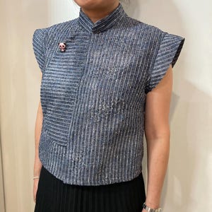 Peut inclure: Haut rayé bleu et argenté avec un col mandarin et des manches courtes. Une petite épingle panda est attachée au haut. Le haut est associé à une jupe plissée noire.