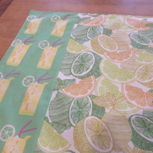 Può includere: Un tessuto verde con un motivo di bevande gialle con cannucce viola e un tessuto bianco con un motivo di limoni e lime verdi e gialli.