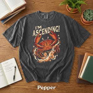 Peut inclure: T-shirt gris fonc&eacute; avec un motif de crabe rouge et orange et le texte "I'M ASCENDING!". Le crabe est entour&eacute; de flammes. Le mot "Pepper" est imprim&eacute; en bas du t-shirt.