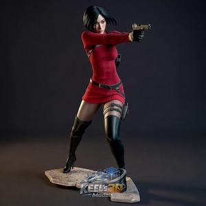 May include: A detailed figurine of a woman in a red dress, black boots, and gloves, holding a gun. The figure is standing on a stone base with a logo. The overall theme is action and gaming.