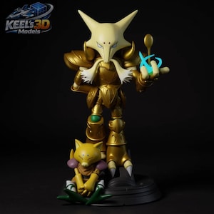 May include: A gold-coloured figurine of a character with a pointed head and armour, holding a spoon and a blue energy effect. A smaller yellow figure sits at the base. The text "KEEL'S 3D MODELS" is in the upper left corner.