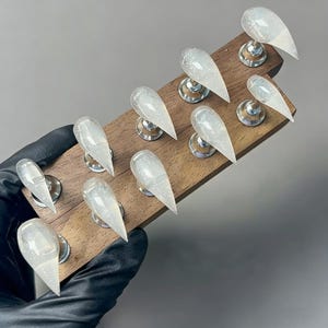 Pode incluir: Um conjunto de dez unhas acrílicas longas e transparentes com detalhes de glitter, exibidas em um suporte de madeira. Cada unha é montada em um pequeno suporte prateado. As unhas têm formato pontiagudo e acabamento brilhante.