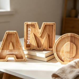 Puede incluir: Objetos decorativos de madera con forma de letras. Las letras tienen forma de A, M y O. La letra A tiene el nombre "Abarca" impreso. La letra M tiene el nombre "McCoy" impreso. La letra O tiene el nombre "Ortega" impreso.