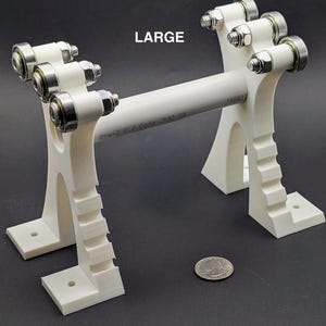 May include: A white, 3D-printed object with multiple roller bearings and a central white tube. The word "LARGE" is printed on the object. The object has a series of steps on the base. A quarter is next to the object.