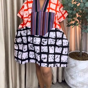 May include: A short-sleeved dress with a vibrant patchwork design. The top features a red and white checkered pattern, transitioning to a striped panel and a black and white checkered skirt. The dress has a V-neck and a loose, comfortable fit.