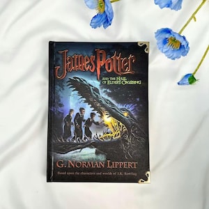 May include: A hardcover book titled "James Potter and the Hall of Elders Crossing" by G. Norman Lippert. The cover features a dark illustration of three figures and a large, shadowy creature. Gold corner protectors are visible.