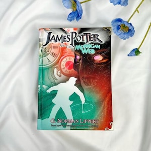 May include: A hardcover book titled "James Potter and the Morrigan Web" with a green, red, and black cover. The cover features a silhouette of a person, clocks, and the author's name, G. Norman Lippert. Blue flowers are in the background.