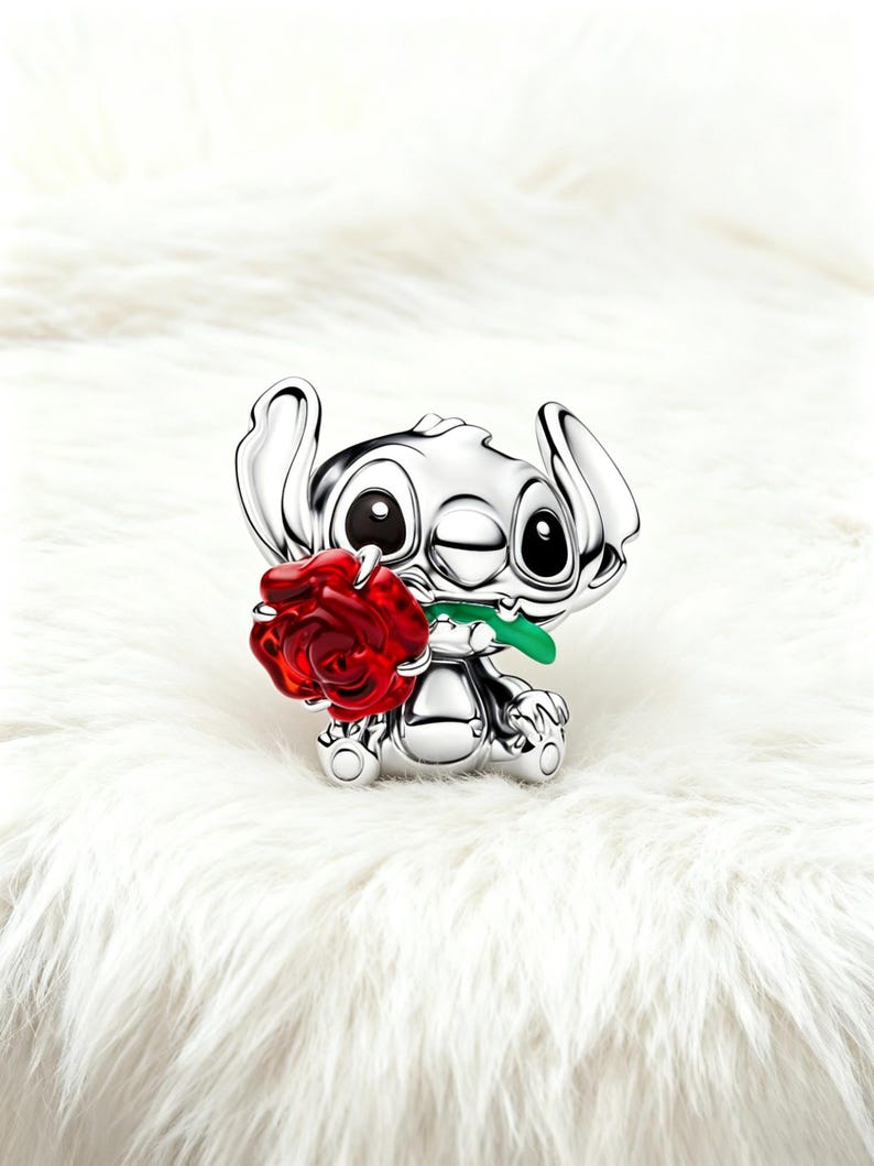 May include: A silver figurine of a cartoon character holding a red rose with a green stem. The character has large black eyes and large ears. The background is a white, fluffy surface.