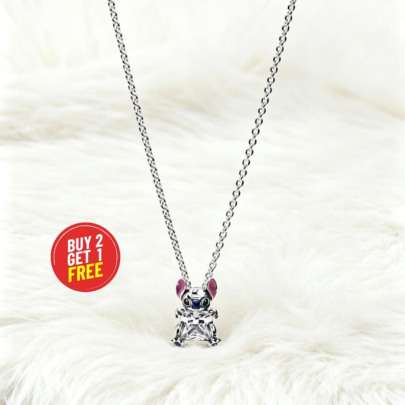 May include: A silver-colored necklace featuring a charm of a cartoon character with blue, pink, and clear accents. The charm is suspended from a delicate chain. A red circle with the text "BUY 2 GET 1 FREE" is in the image.