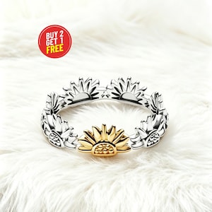 May include: A silver-toned ring featuring a repeating sunflower motif around the band. One sunflower is finished in a gold tone, while the others are silver. A red circular graphic in the upper left corner contains the text BUY 2 GET 1 FREE.