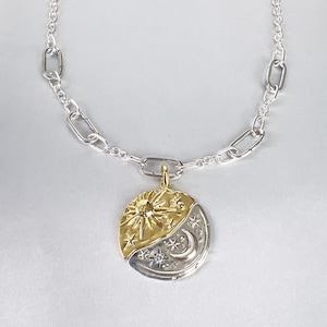 May include: A silver chain necklace featuring a round, two-toned pendant. The top half is gold-colored with a sun and star motif, while the bottom half is silver-colored with a crescent moon and star design, including a small embedded clear stone.