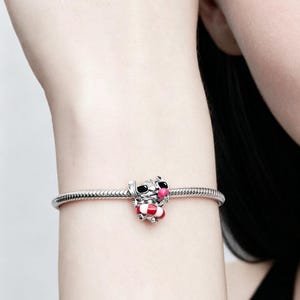 May include: A silver charm bracelet with a colorful charm. The charm is a cartoon character wearing sunglasses and a life preserver. The charm has red, white, pink, and black accents.