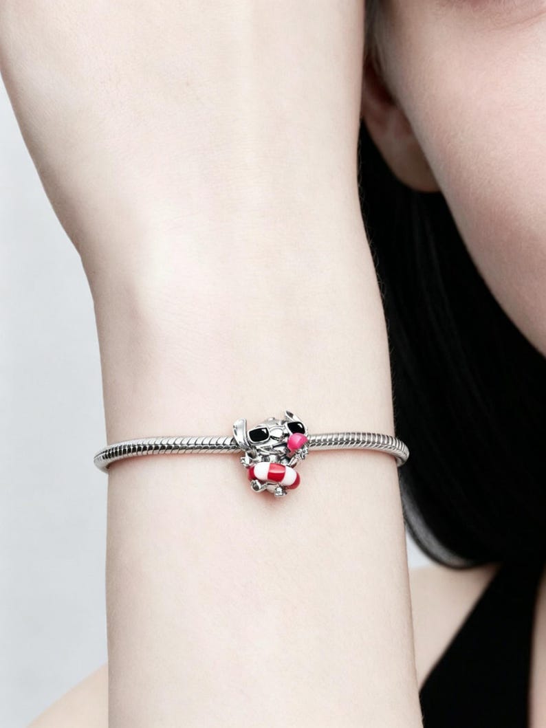 May include: A silver charm bracelet with a colorful charm. The charm is a cartoon character wearing sunglasses and a life preserver. The charm has red, white, pink, and black accents.