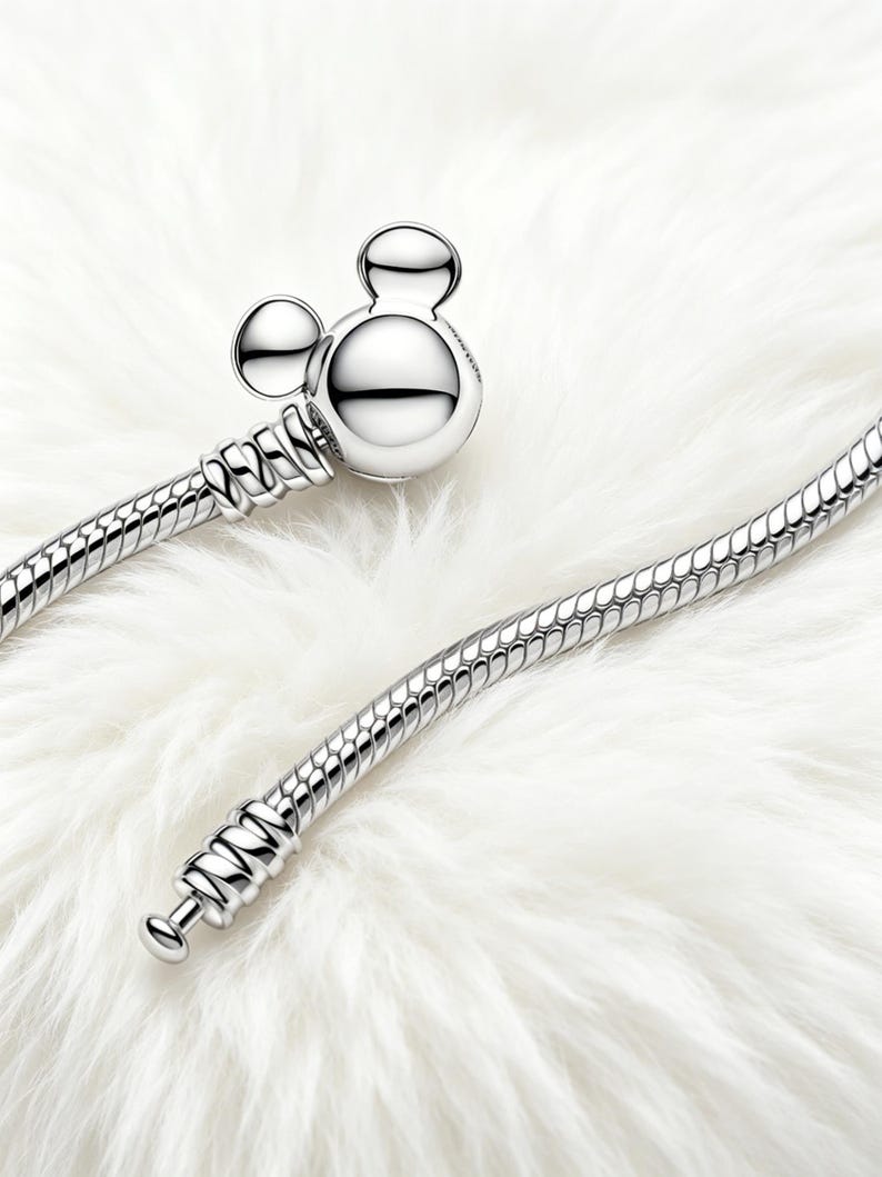 Peut inclure: Un bracelet argent&eacute; avec un fermoir en forme de Mickey Mouse. Le bracelet pr&eacute;sente un motif de cha&icirc;ne serpent. Le fermoir est compos&eacute; d'une t&ecirc;te ronde et de deux petites oreilles rondes. Le bracelet est pr&eacute;sent&eacute; sur une surface blanche et duveteuse.