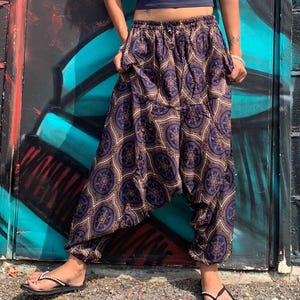 May include: Loose-fitting harem pants featuring a dark blue and gold geometric circular pattern. The trousers have an elasticized waistband, a low-slung drop crotch design, and elastic cuffs at the ankles, creating a relaxed and voluminous silhouette.